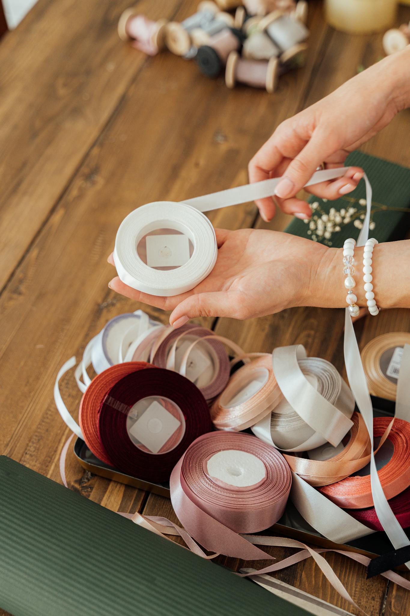 Hand arranging colorful ribbons for crafts on a wooden table, showcasing creativity and elegance.